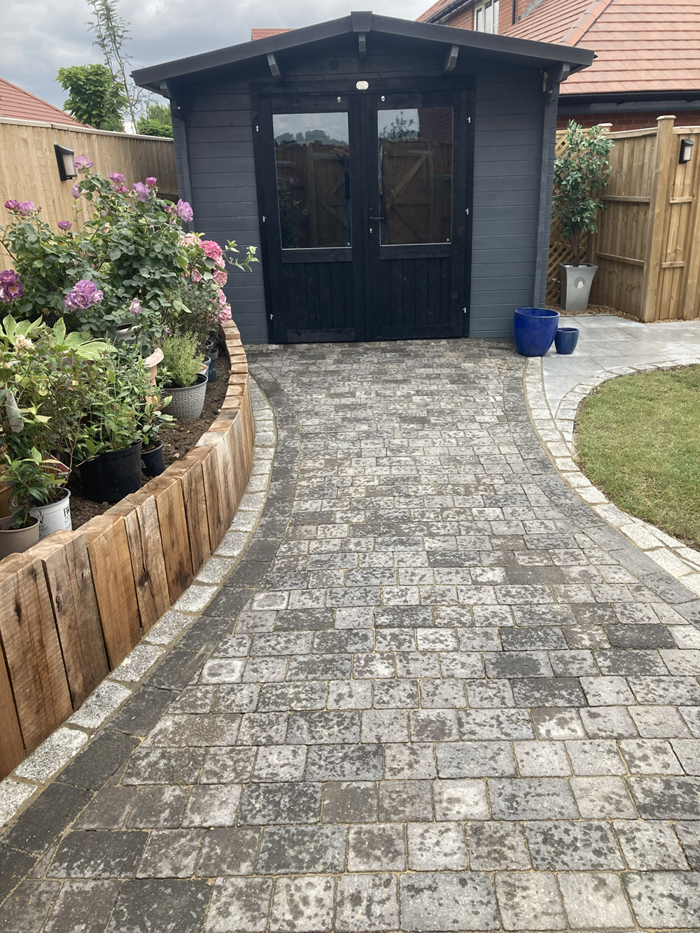 Weathered grey block paving path with cream borders and timber planter beds